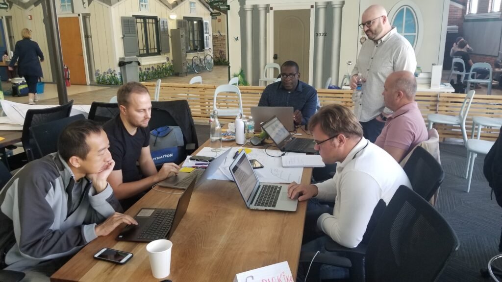 Participants collaborate around laptops and notes during a facilitated working session.